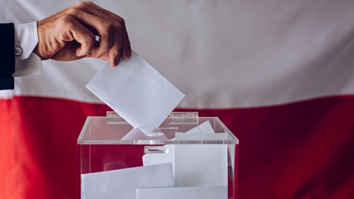 Wyborca wrzucający kartę do głosowania do urny, w tle polska flaga